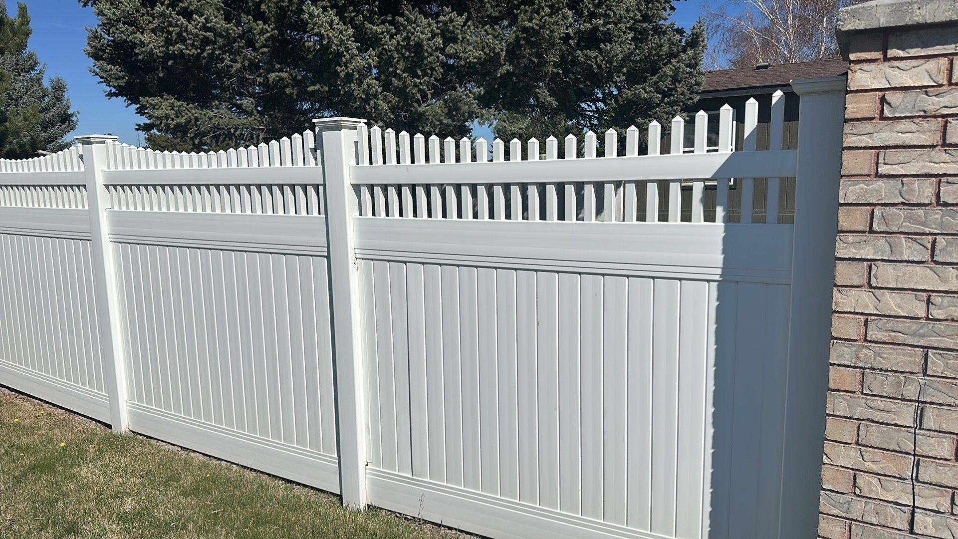 A white fence is sitting next to a brick wall.