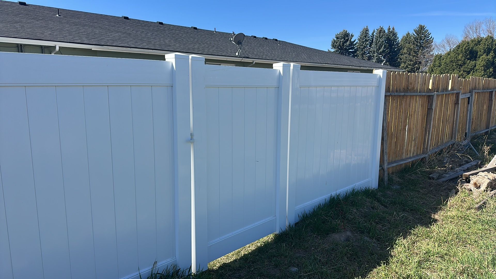 A white fence is sitting in the grass next to a house.