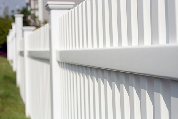 A close up of a white vinyl fence in a yard.
