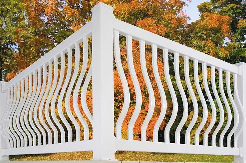 A white fence with a swirl design and trees in the background