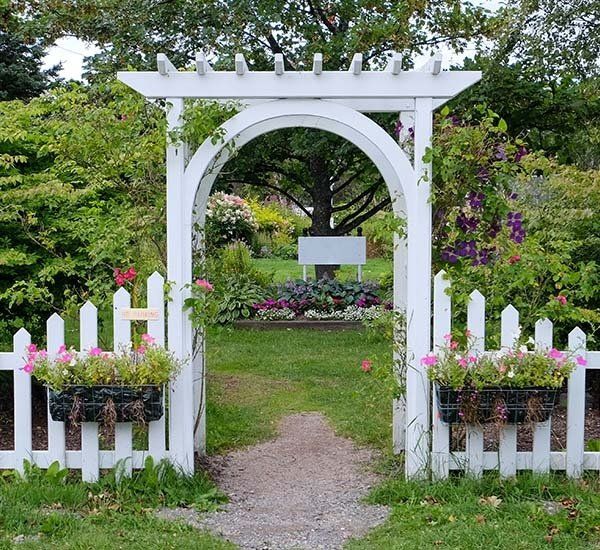A white archway with a white picket fence leading to a garden