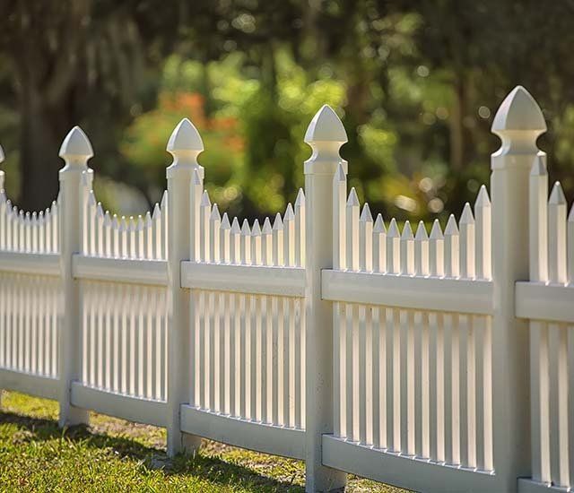 A white picket fence is sitting on top of a lush green field.
