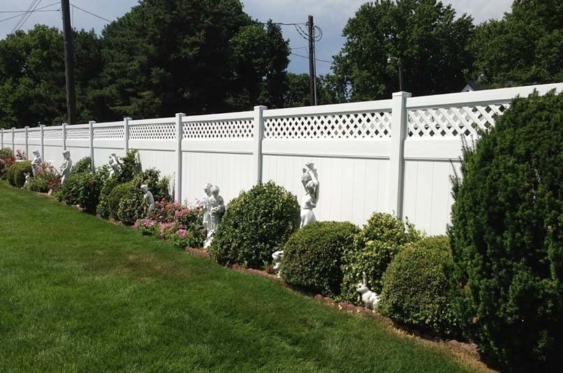 A white fence is surrounded by bushes and flowers