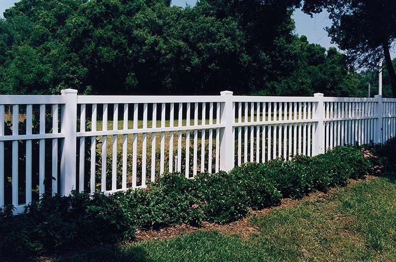 A white fence surrounds a grassy area with trees in the background