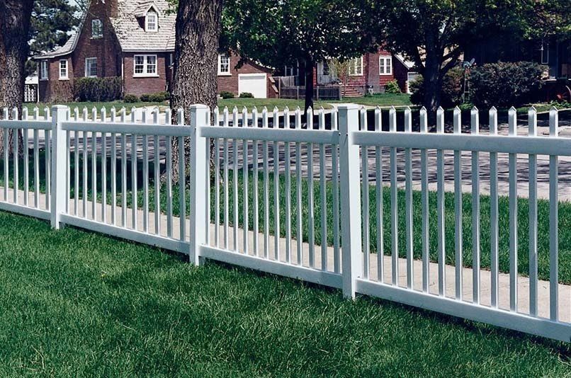 A white fence surrounds a lush green yard in front of a house