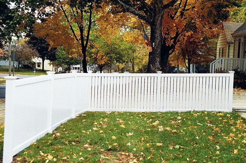 A white fence surrounds a lush green yard with trees in the background.