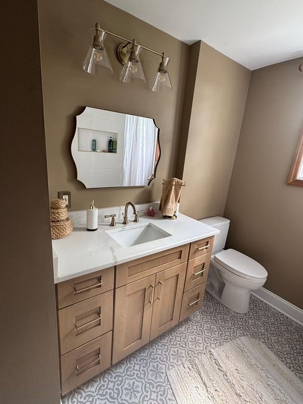 Small bathroom with wood vanity, white sink, mirror, toilet, and woven decor in neutral tones.