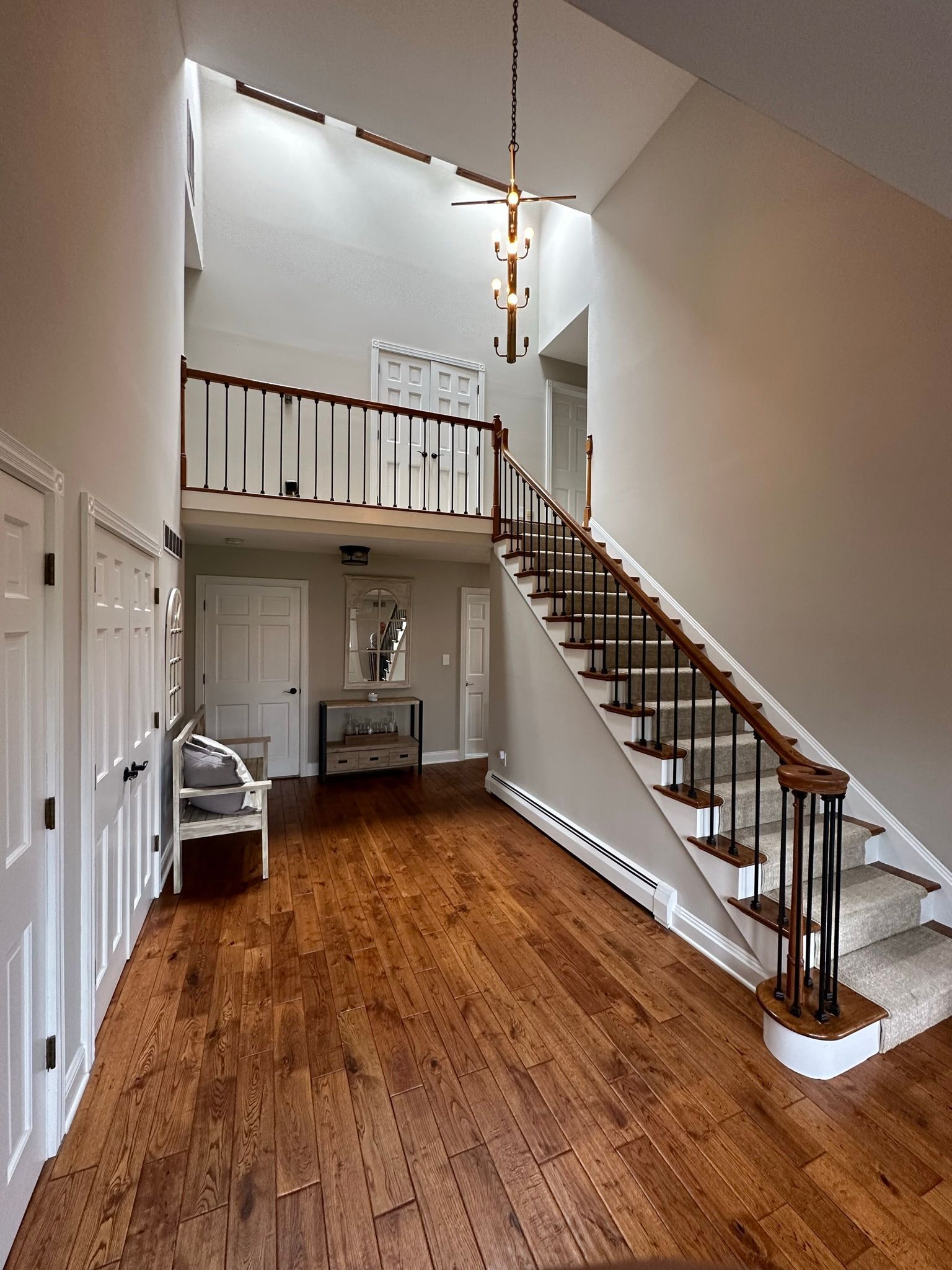 Foyer with hardwood floor, staircase, and second-floor balcony. Light fixtures hang from the high ceiling.