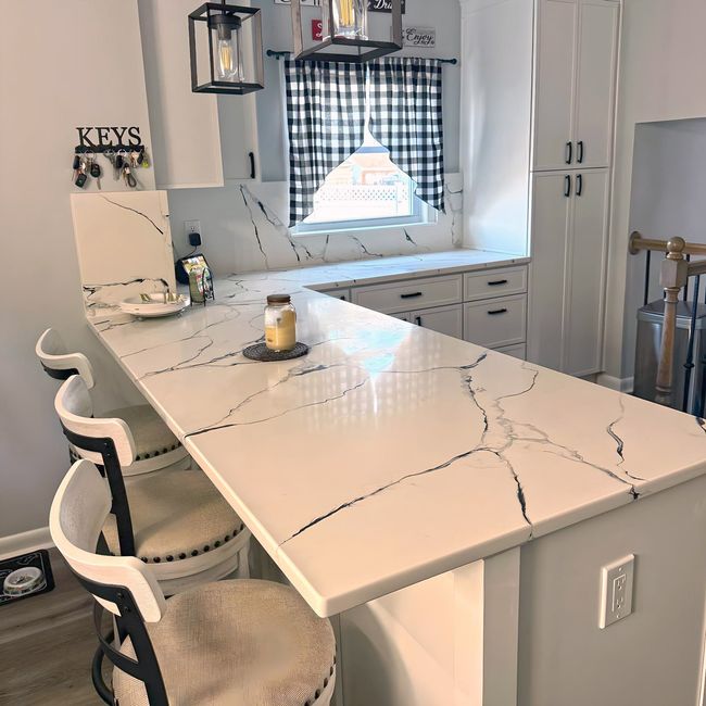 Bright kitchen with white cabinets, blue island, gold light fixtures, and marble backsplash.