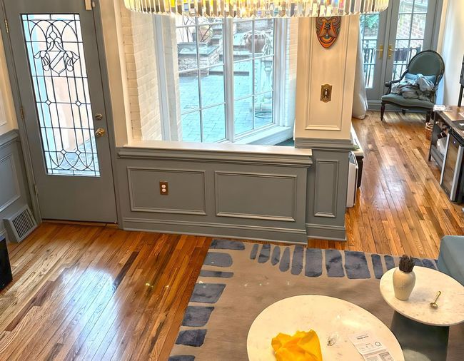 Spacious living room with high ceilings, wood floors, and large windows overlooking trees.