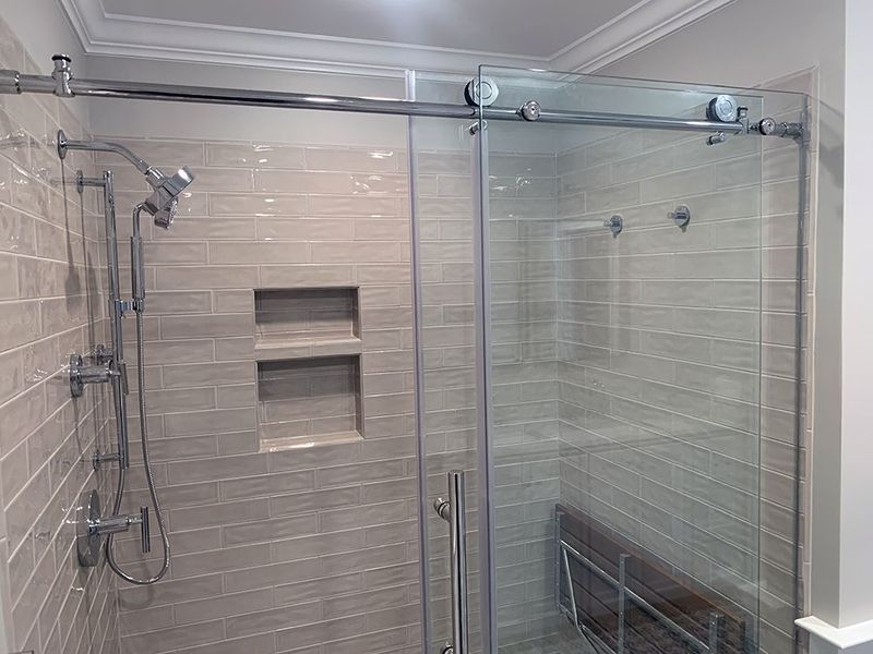 Glass-enclosed shower with sliding door, gray tiled walls, chrome fixtures, and built-in shelf.