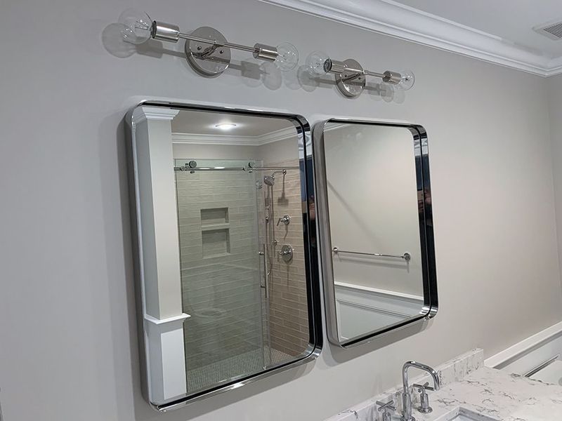 Bathroom with two mirrors, chrome light fixtures, and a glass-enclosed shower.