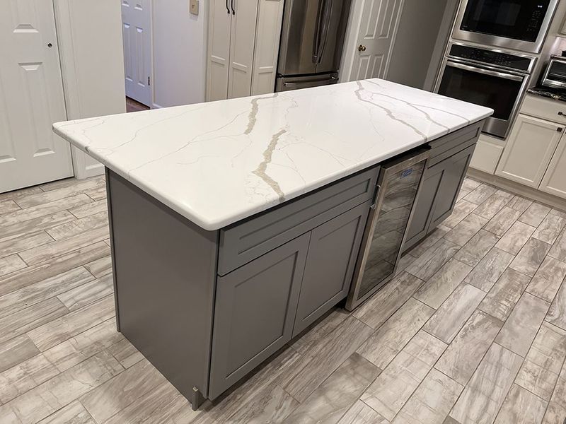 Gray kitchen island with white countertop, built-in wine cooler, and cabinets.