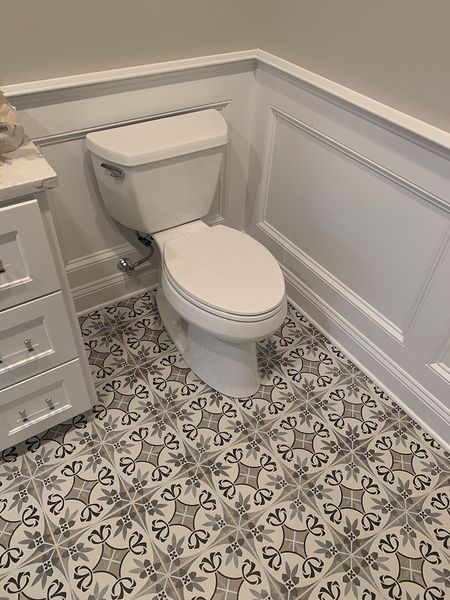 Toilet in a small bathroom with patterned tile floor, white wainscoting, and a white vanity.