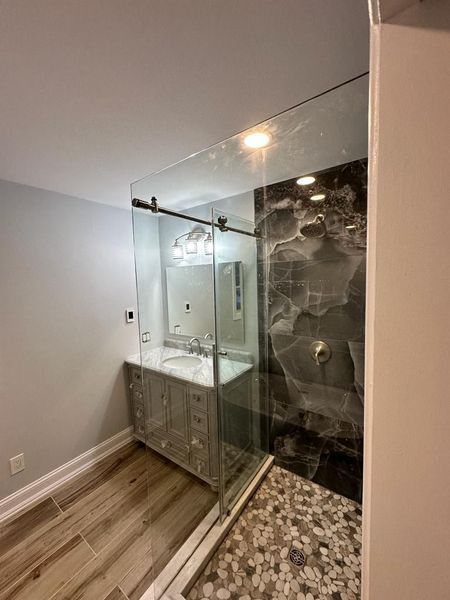 Bathroom with a glass shower, vanity, and pebble floor. Gray, white, and wood tones.