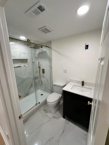 Newly renovated bathroom with marble-look tile, glass shower, black vanity, and gold fixtures.