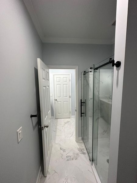 Bathroom hallway with light gray walls, white trim, marble tile floor, and a glass shower.