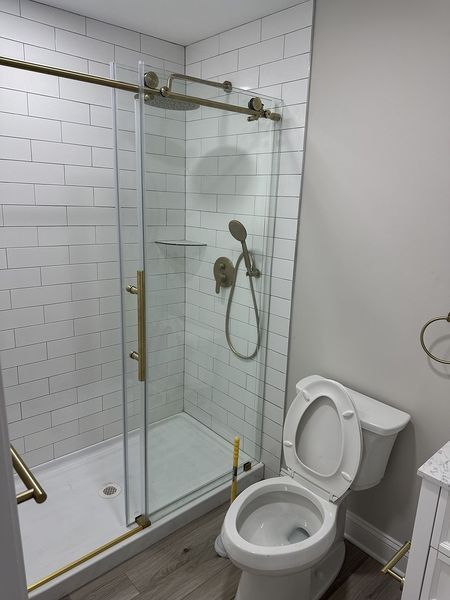 Bathroom with white tile shower, sliding glass door, gold fixtures, and toilet.