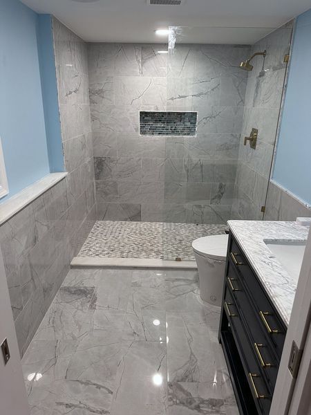 Bathroom with gray marble tile shower and flooring, pebble shower floor, blue walls, dark vanity.