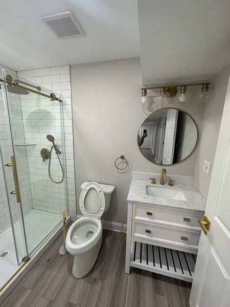 A newly renovated bathroom with a white shower, toilet, and vanity with gold hardware.