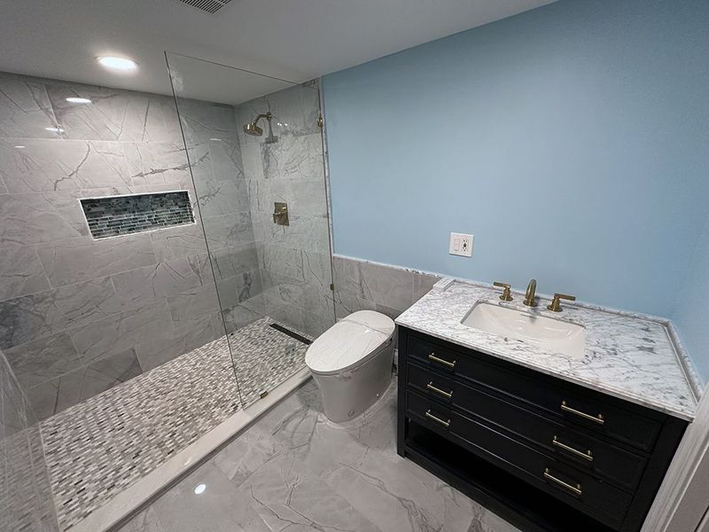 Modern bathroom with a tiled shower, toilet, black vanity, and light blue walls.