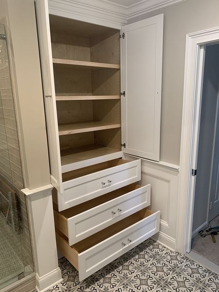Built-in white storage cabinet in a bathroom with open doors and drawers.
