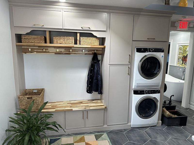 Laundry room with stacked washer/dryer, built-in storage, bench, and woven baskets.