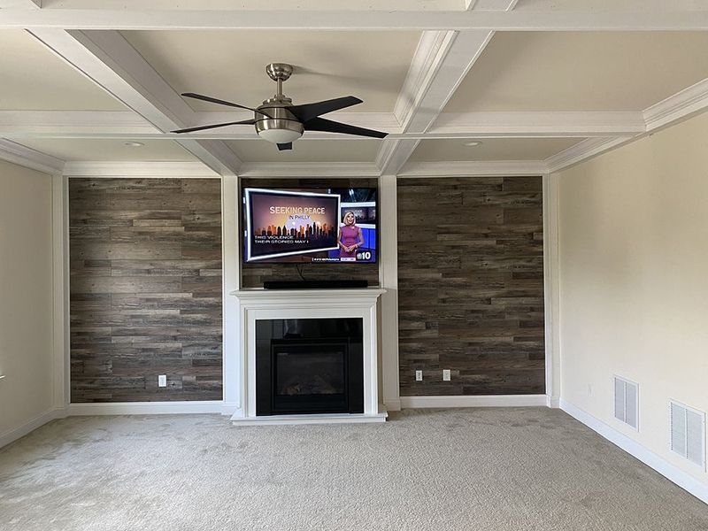 Living room with a fireplace, TV, wood paneling, and a ceiling fan.