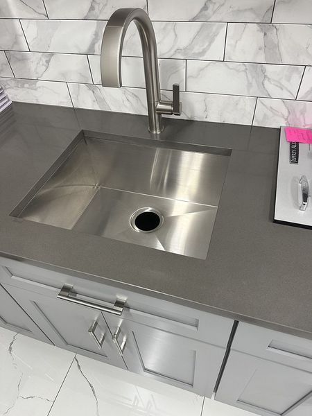 Stainless steel kitchen sink in a gray countertop, with gray cabinets below, and a faucet.