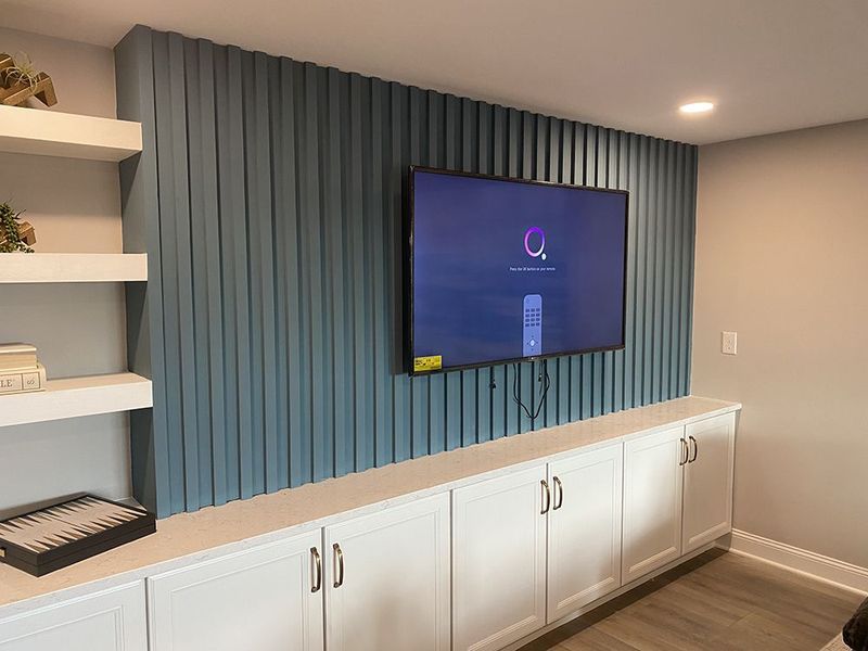 Blue vertical paneling with mounted TV, white built-in storage cabinets, and floating shelves.