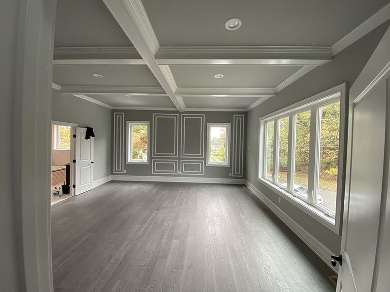 Empty room with gray walls, wood floor, white trim, and large windows.