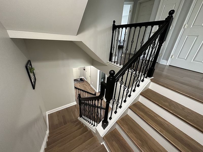 Staircase with wooden steps, black railing, leading down to a hallway. Gray walls, white trim.