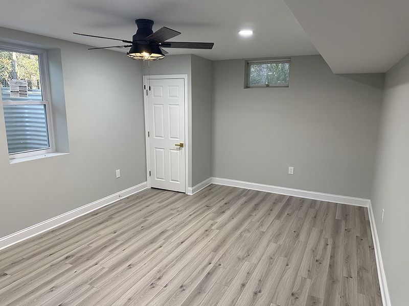 Empty room with gray walls, light wood-look floor, window, and closed white door.