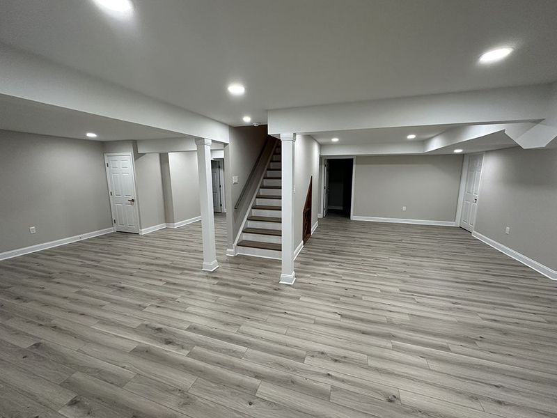 Finished basement with gray walls, wood-look flooring, and a staircase.