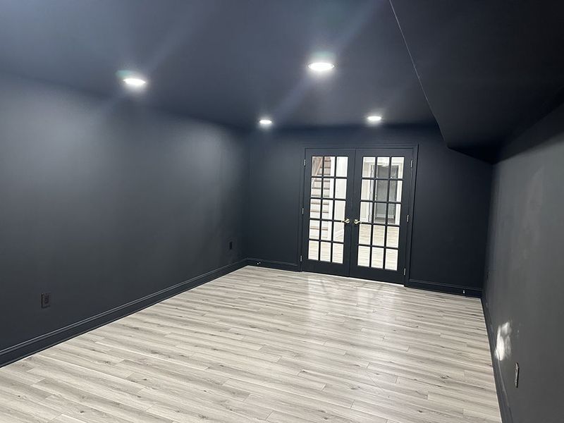 Empty room with gray wood-look floor, black walls, ceiling, and French doors; recessed lights.