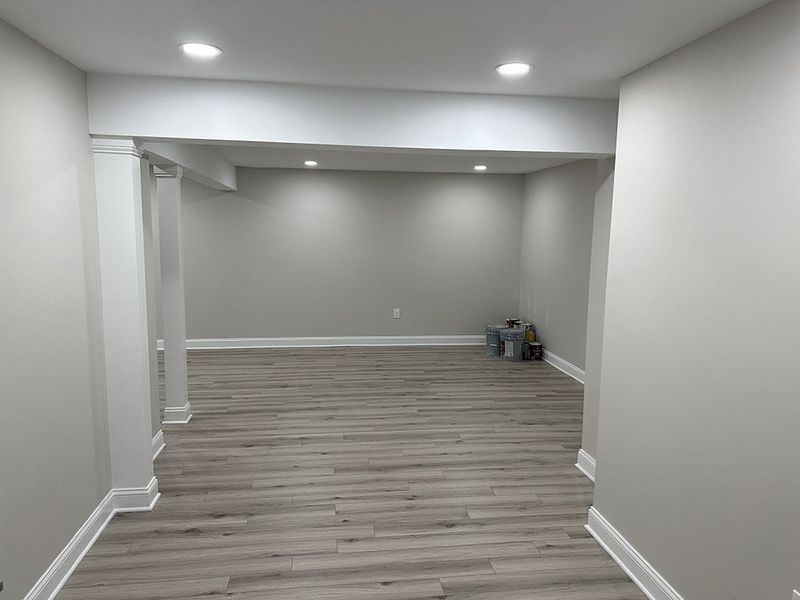 Empty room with gray walls, white trim, recessed lighting, and wood-look flooring.
