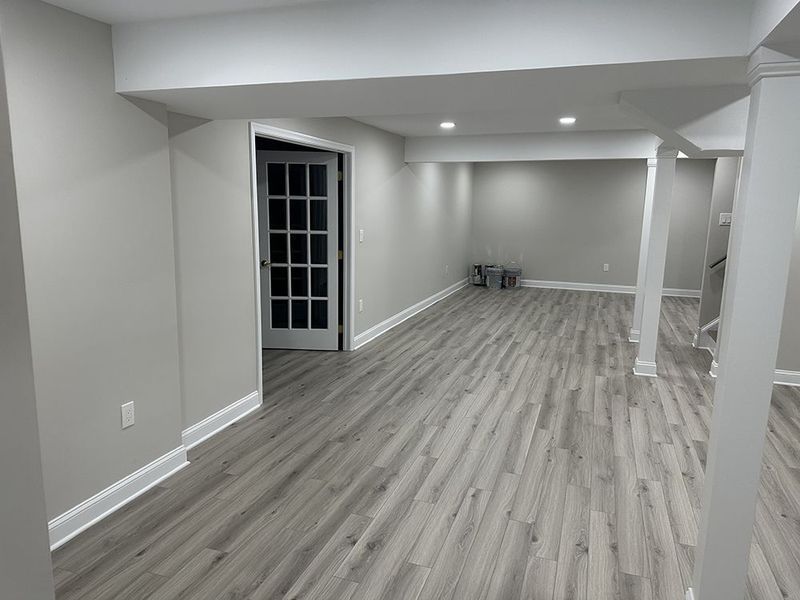 Empty renovated basement with gray wood-look flooring, light gray walls, and white trim.