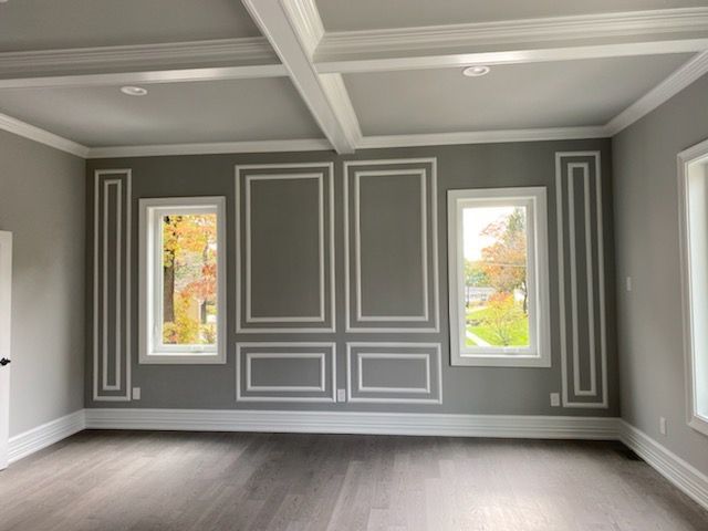 Gray room with white molding and windows, wooden floor, decorative ceiling beams.