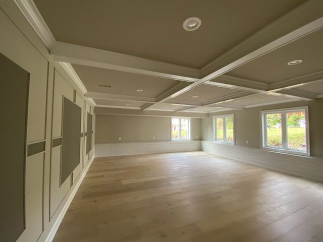Empty room with light wood floors, coffered ceiling, and wainscoting. Beige and white tones.