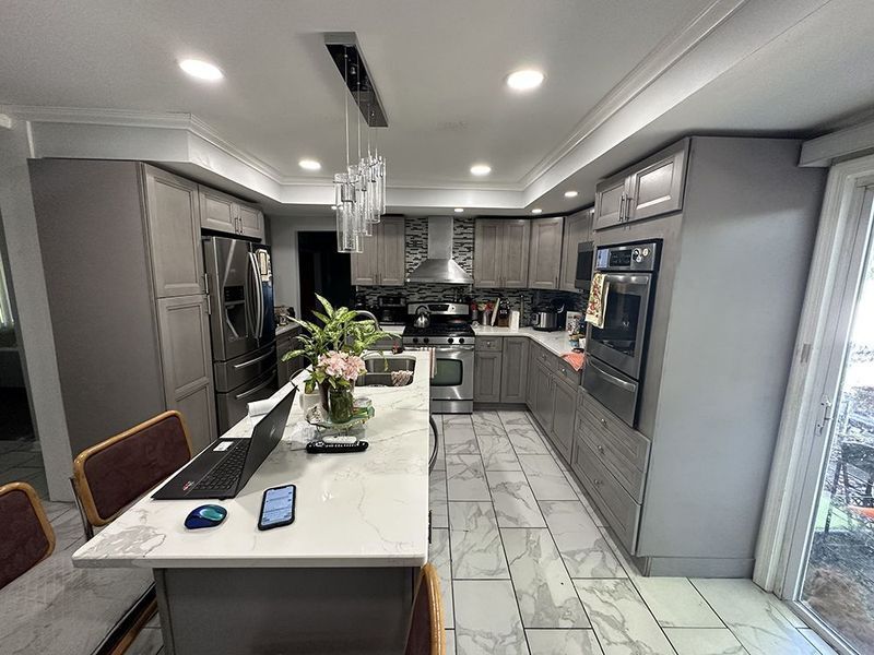 Modern kitchen with gray cabinets, white countertops, stainless steel appliances, and a central island.