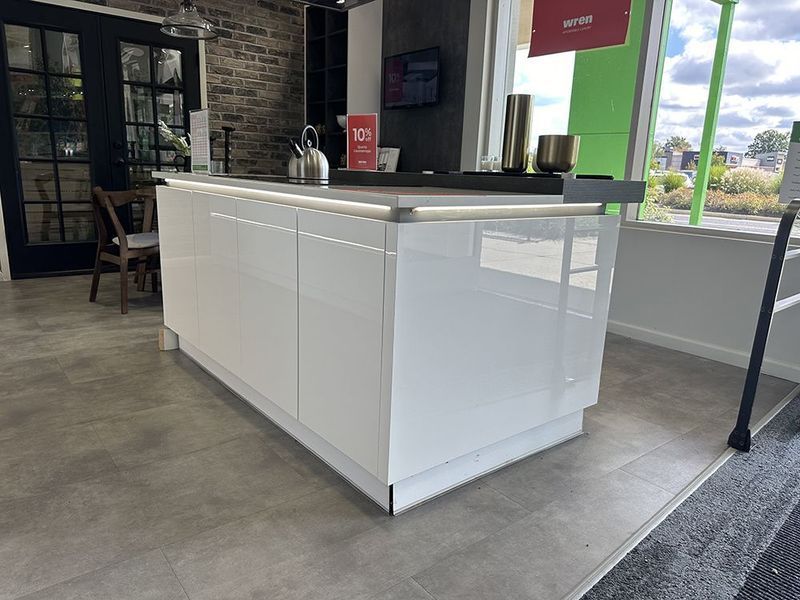 White kitchen island with glossy finish and dark countertop, displayed in showroom.
