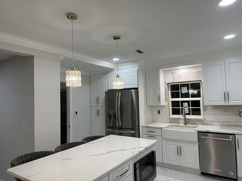 Kitchen with white cabinets, island, and pendant lights. Stainless steel appliances and a farmhouse sink.