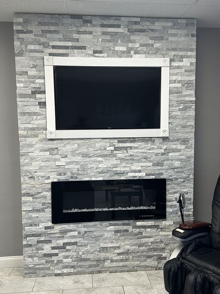 Gray brick wall with a mounted TV and electric fireplace.