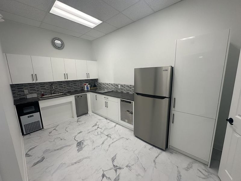 Modern office kitchen with white cabinets, stainless steel appliances, and marble flooring.