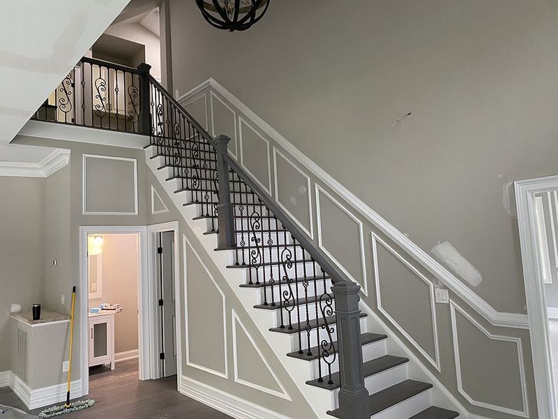 A staircase with gray steps and trim, iron railing, and a light gray wall.
