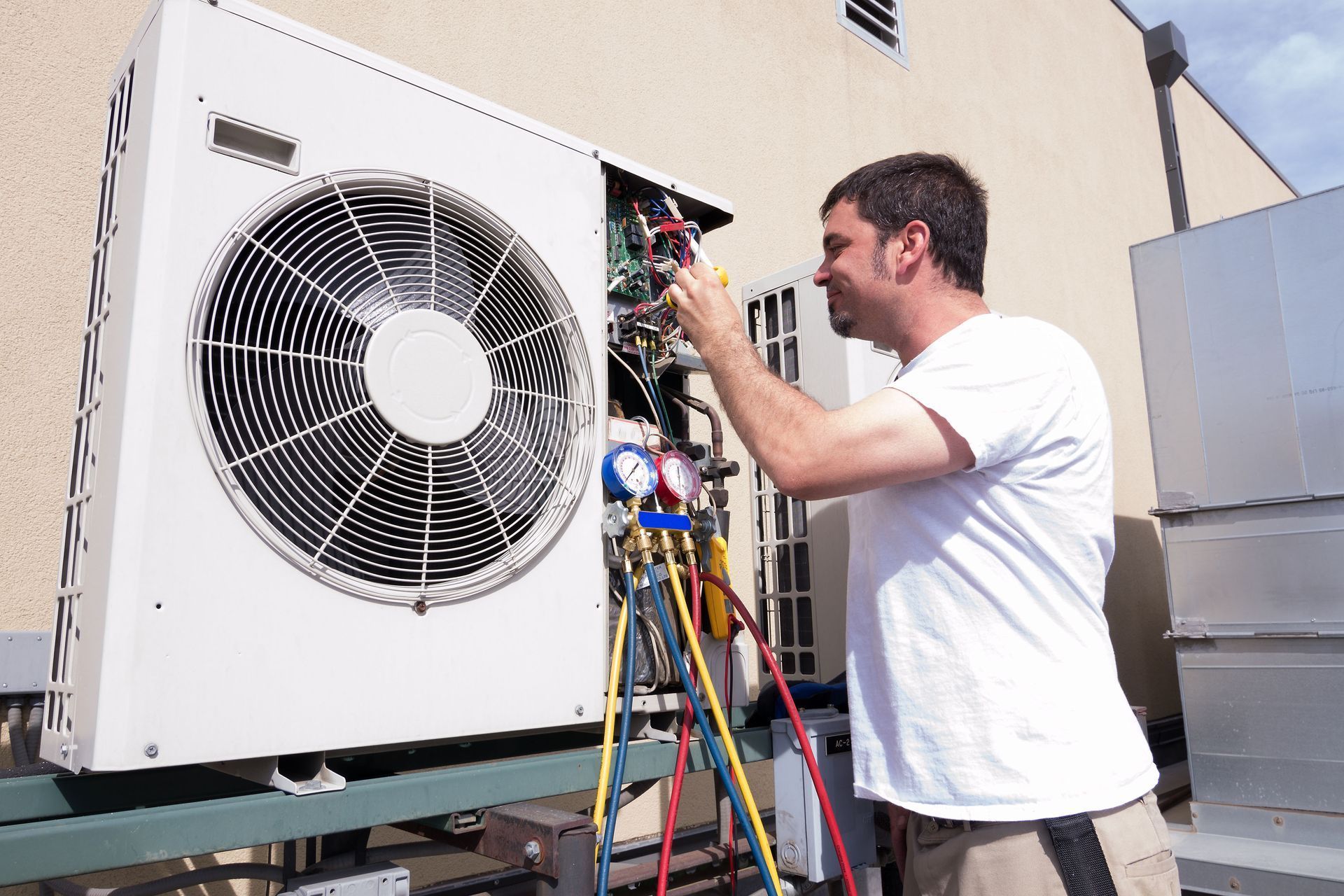 HVAC technician repairing an air conditioning unit outside. He is using tools and gauges.