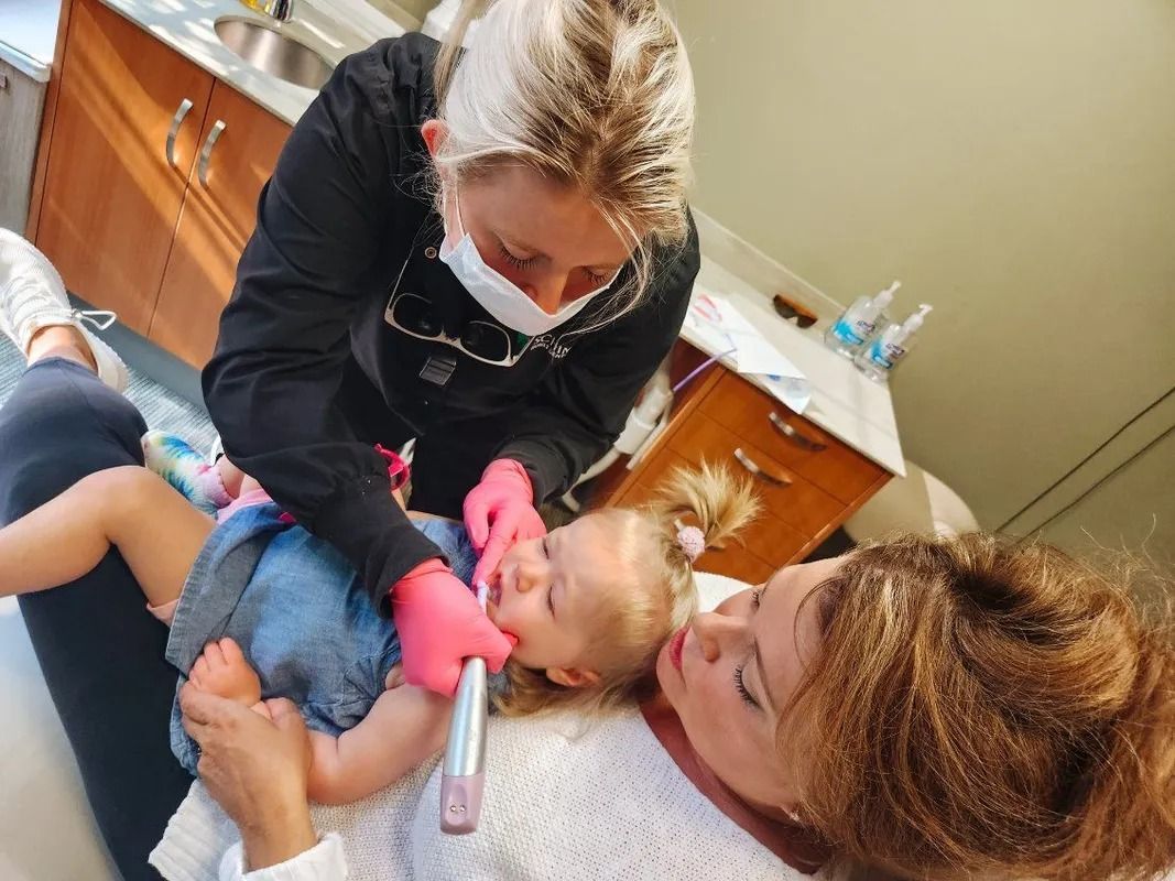 Dentist examining a child's teeth while the child is held by a person lying on a dental chair.
