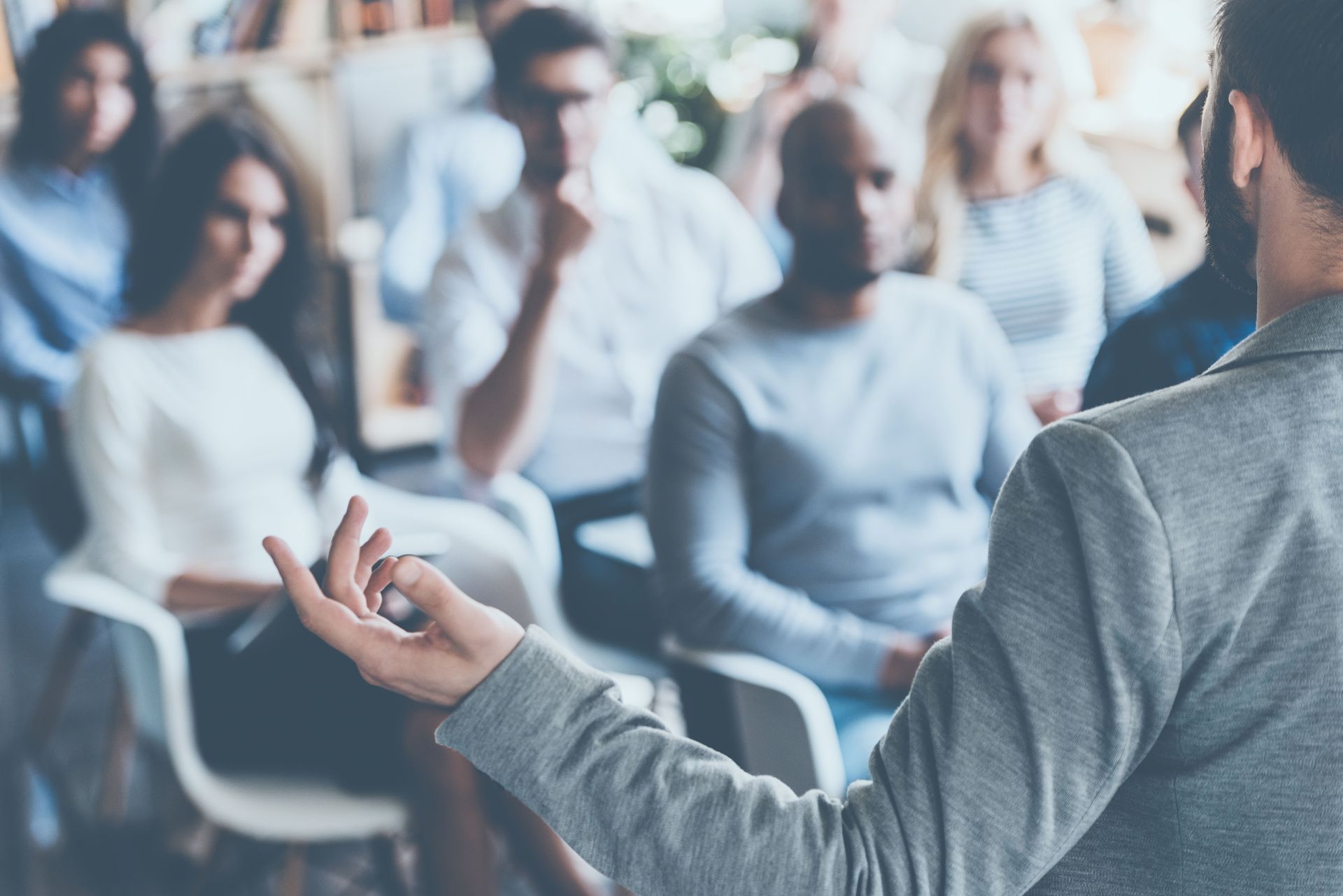 Person giving a presentation to a seated group. They're gesturing, and people listen attentively.