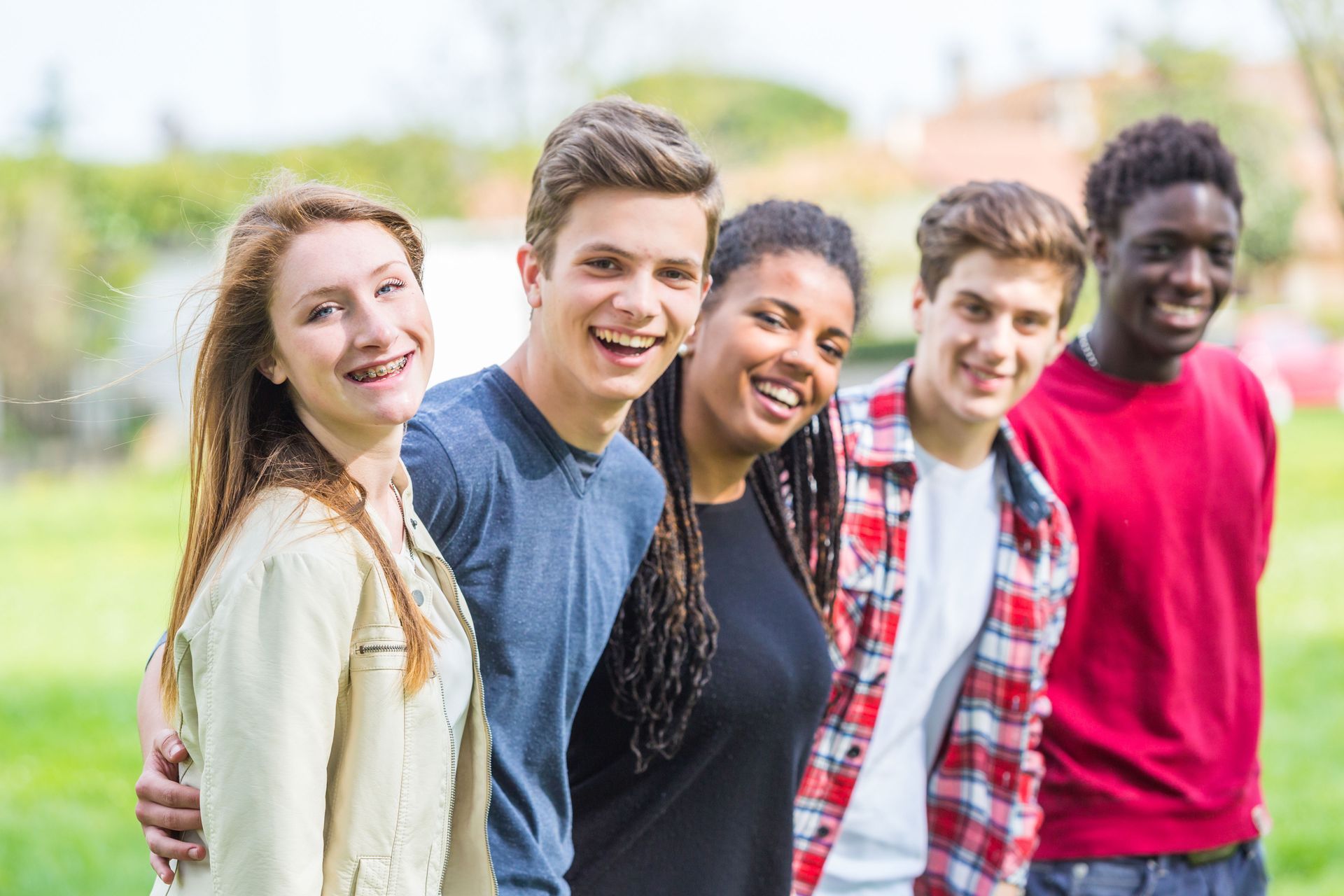 Group of smiling young people outdoors with arms around each other.