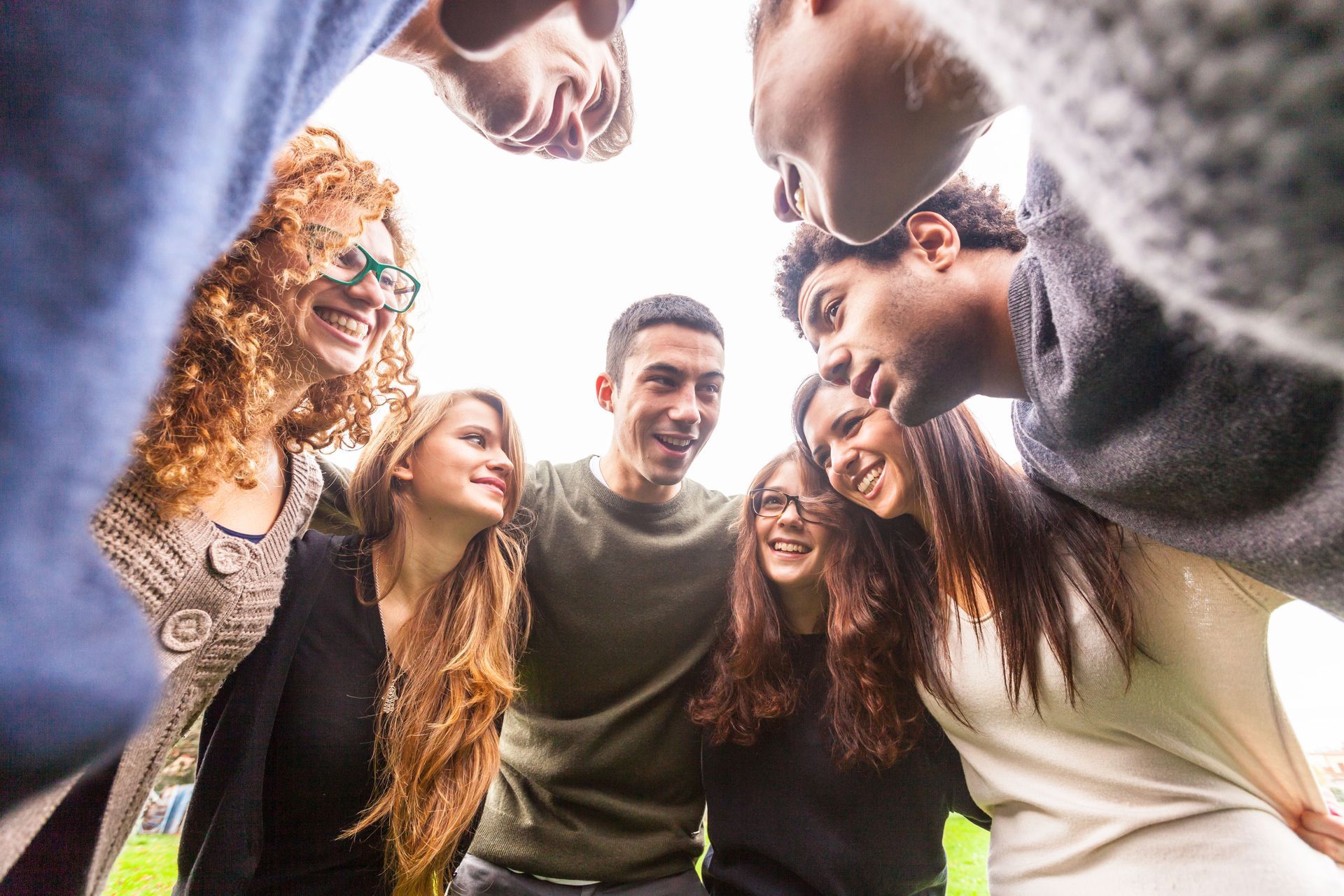 Group of people huddling closely, smiling with arms around each other. View from below, looking upward.